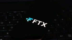 FTX logo displayed on a smartphone with a black background and the phone resting on the black keyboard