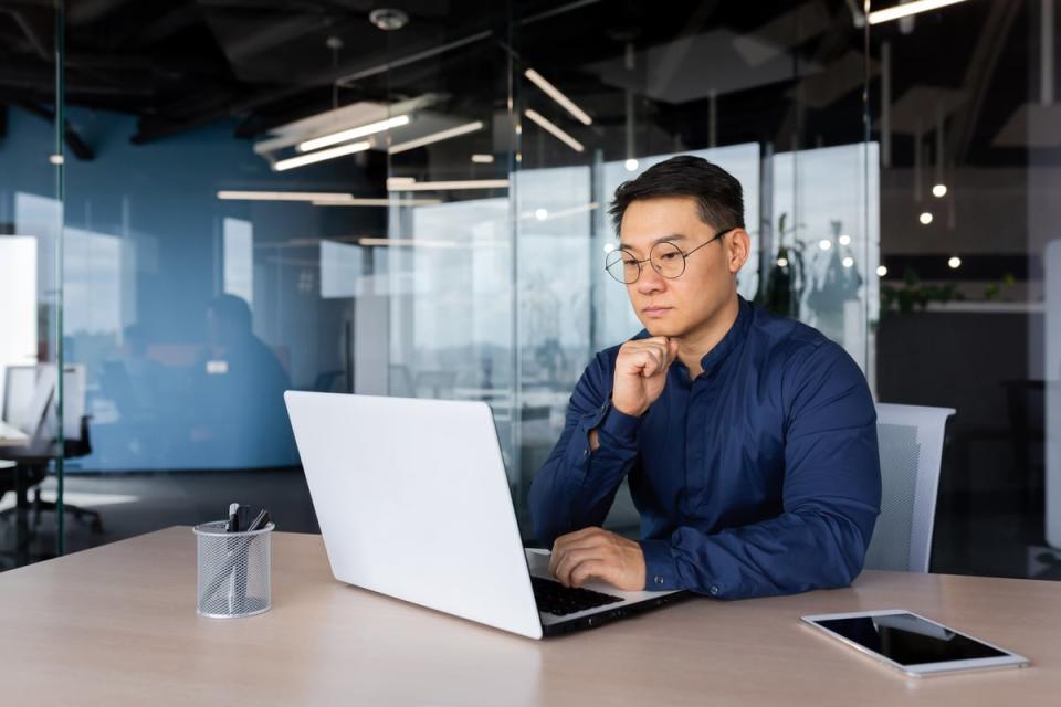 A person looks thoughtfully at a laptop.